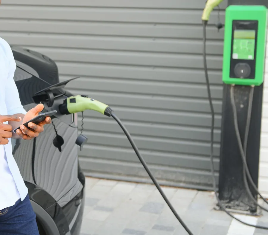 Driver checking a phone beside an EV plugged into a charging station