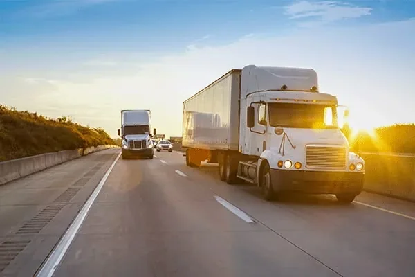 Two haulage trucks travelling a highway at sunset