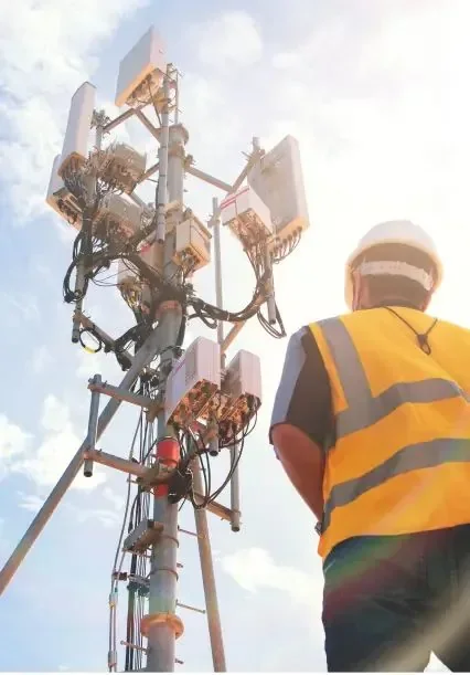 Technician in a hard hat looking up at a telecom mast