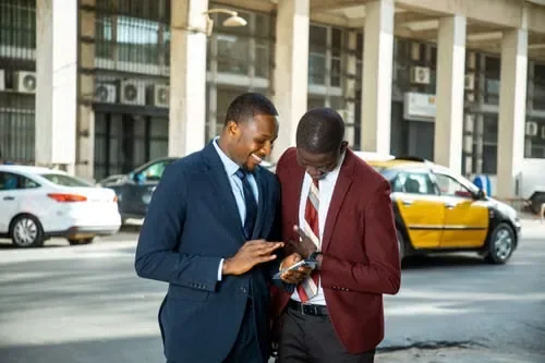Two colleagues smiling over a phone in the street